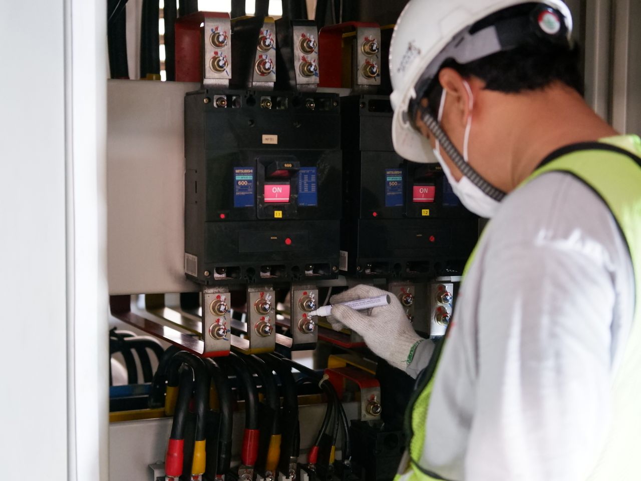 Services-01 Technician wearing safety gear inspecting electrical panels in an industrial setting.