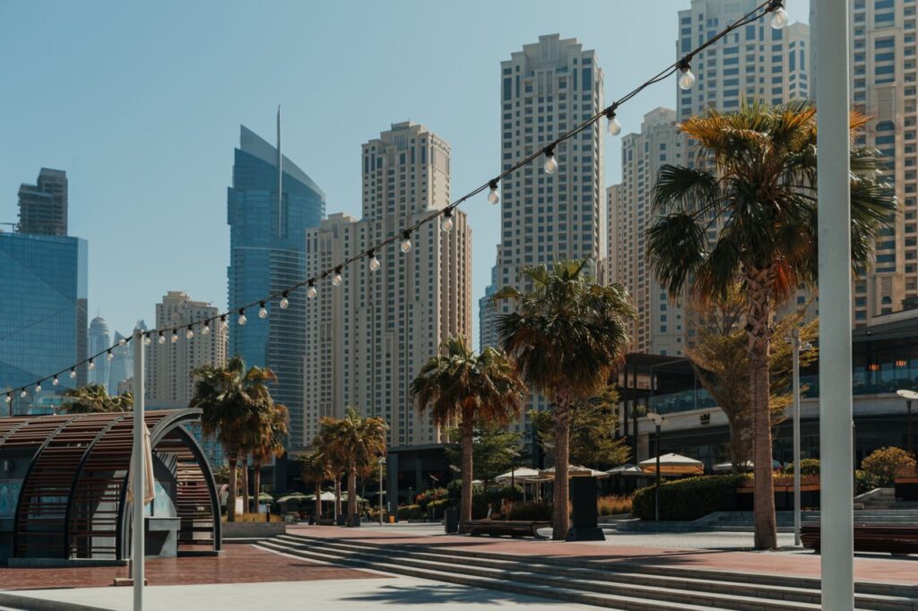 pexels photo 27277169 Urban skyline of Dubai with modern buildings and palm trees under a bright sky.