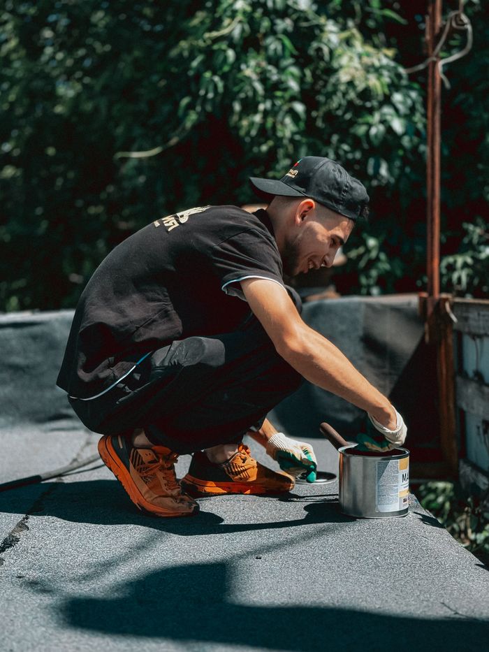 Projects Young man in casual attire applying sealant to a rooftop on a sunny day, emphasizing outdoor labor.