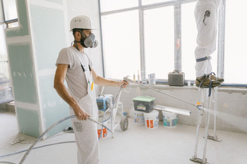 pexels photo 5493664 Two construction workers wearing protective gear and painting interior walls for a renovation project.